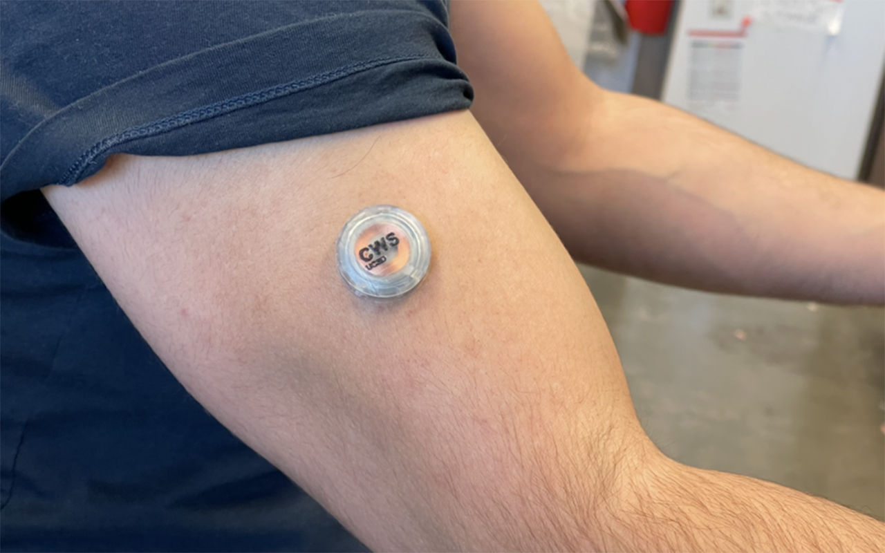 人の上腕に装着するボタン状の電子機器。